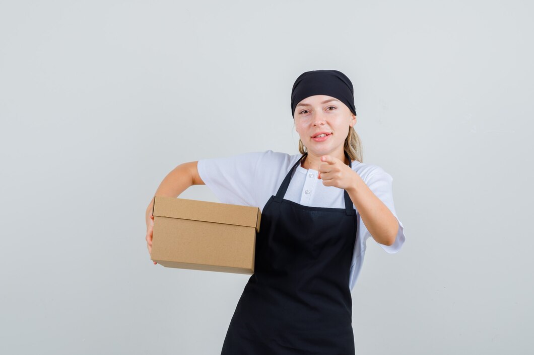 young-waitress-pointing-while-holding-box-uniform-apron-looking-cheery_176474-18214.jpg