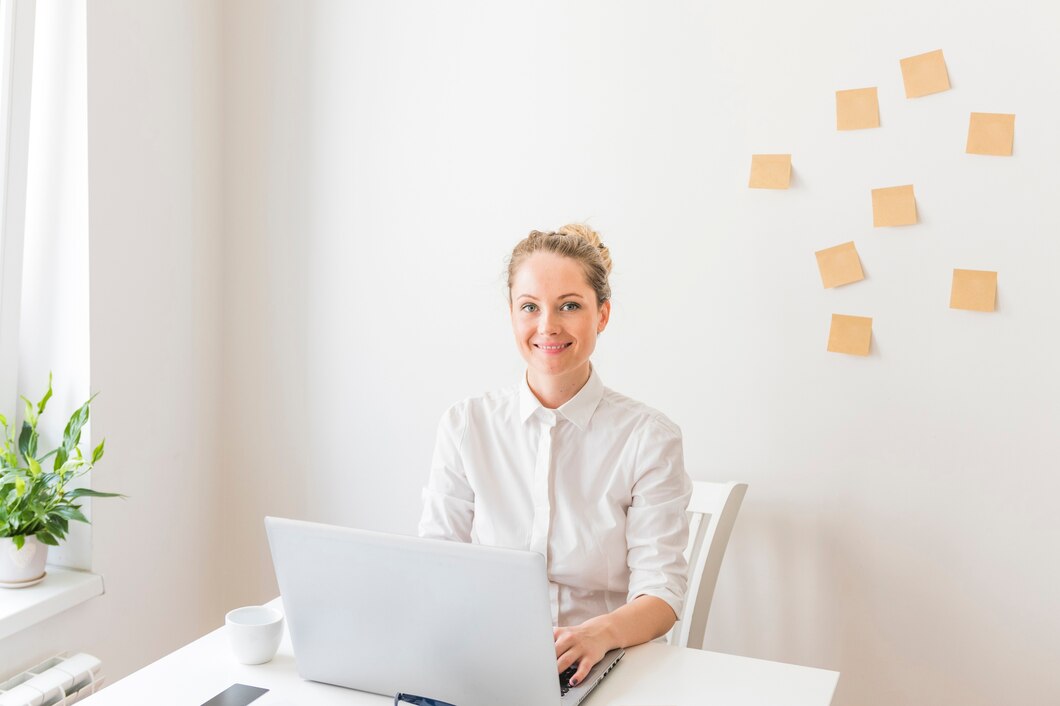 smiling-businesswoman-using-laptop-with-sticky-notes-wall_23-2147880575.jpg